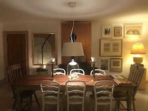 A dining room with a wooden table, white chairs, a chandelier, and framed artwork on the walls.