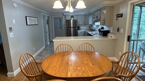 Un comedor con una mesa redonda de madera y cuatro sillas, una cocina con armarios blancos y una lámpara en el techo.