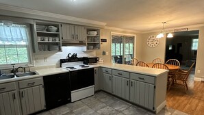 Una cocina con gabinetes grises, lavavajillas, estufa y un comedor con sillas de madera y una mesa.
