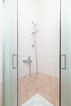A shower with a handheld showerhead and a fixed wall-mounted showerhead, a glass door, and a corner bathtub. - Apartment Tena (Ližnjan)