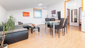 A modern living room with a glass dining table, black chairs, a grey sofa, and a potted plant. - Apartment Tena (Ližnjan)