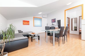 A modern living room with a glass dining table, black chairs, a grey sofa, and a potted plant. - Apartment Tena (Ližnjan)