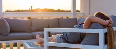 Una persona recostada en un sofá blanco al aire libre, con vista al atardecer.
