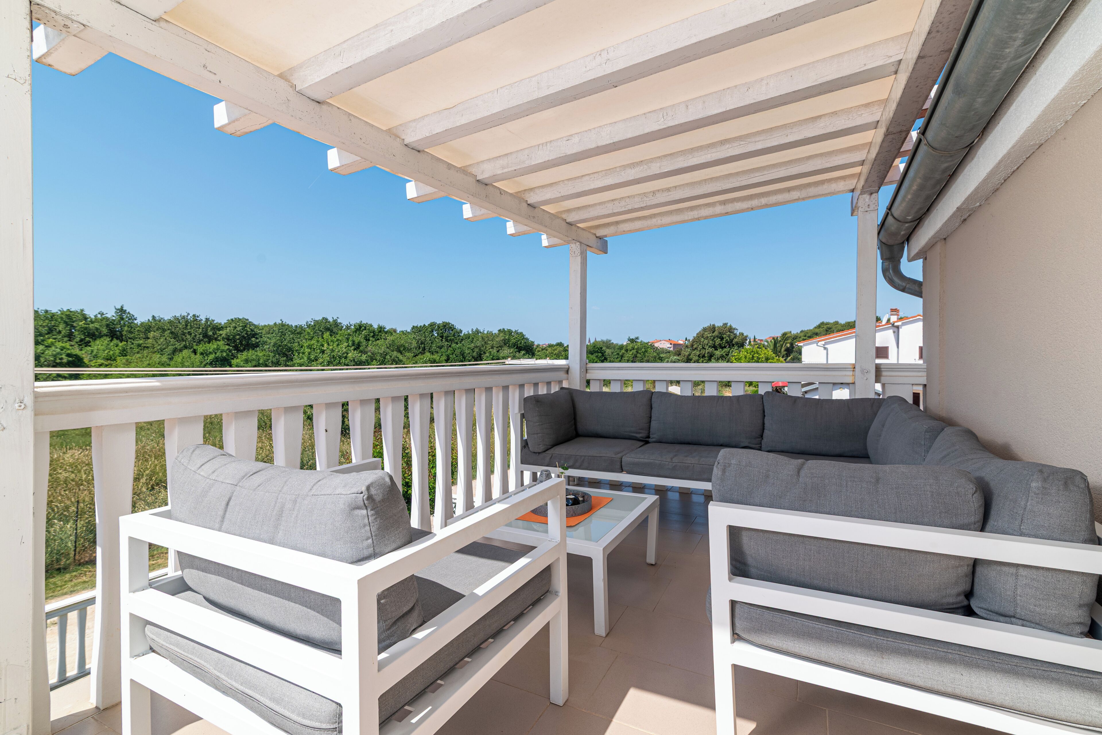 A covered outdoor seating area with white furniture and a view of the landscape.