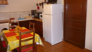 Eine kompakte Küche mit Mikrowelle, Toaster und Kühlschrank. Ein Holztisch mit bunten Tischdecken liegt im Vordergrund.