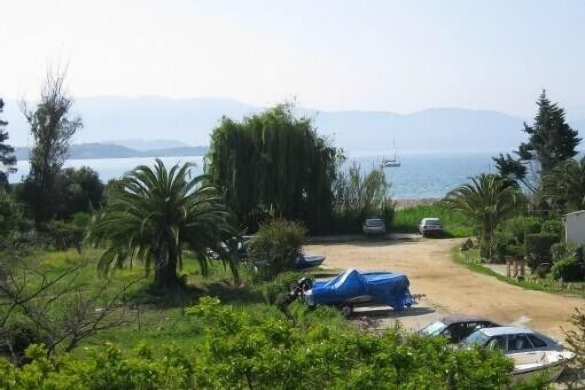 A coastal property with a dirt driveway leading to a covered car and a parked car.