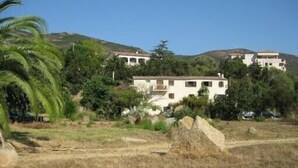 A white building with multiple balconies, surrounded by greenery and hills. - F3 feet in the water. 50 m from the beach (Sagone)