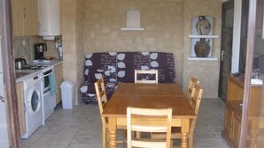 A compact kitchen with a washing machine, a dining table with chairs, and a sofa with a patterned cushion. - F3 feet in the water. 50 m from the beach (Sagone)