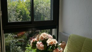 Une chambre avec un lit, une fenêtre donnant sur un paysage verdoyant et un vase rempli de fleurs.