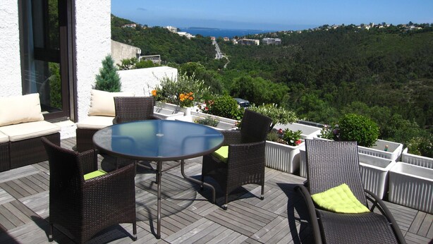 Une terrasse dotée de meubles en osier et d’une table en verre, offrant une vue sur un paysage côtier.