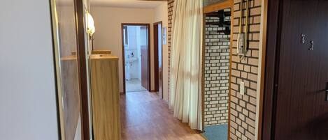Un pasillo con suelo de madera, pared de ladrillo y puerta de madera.