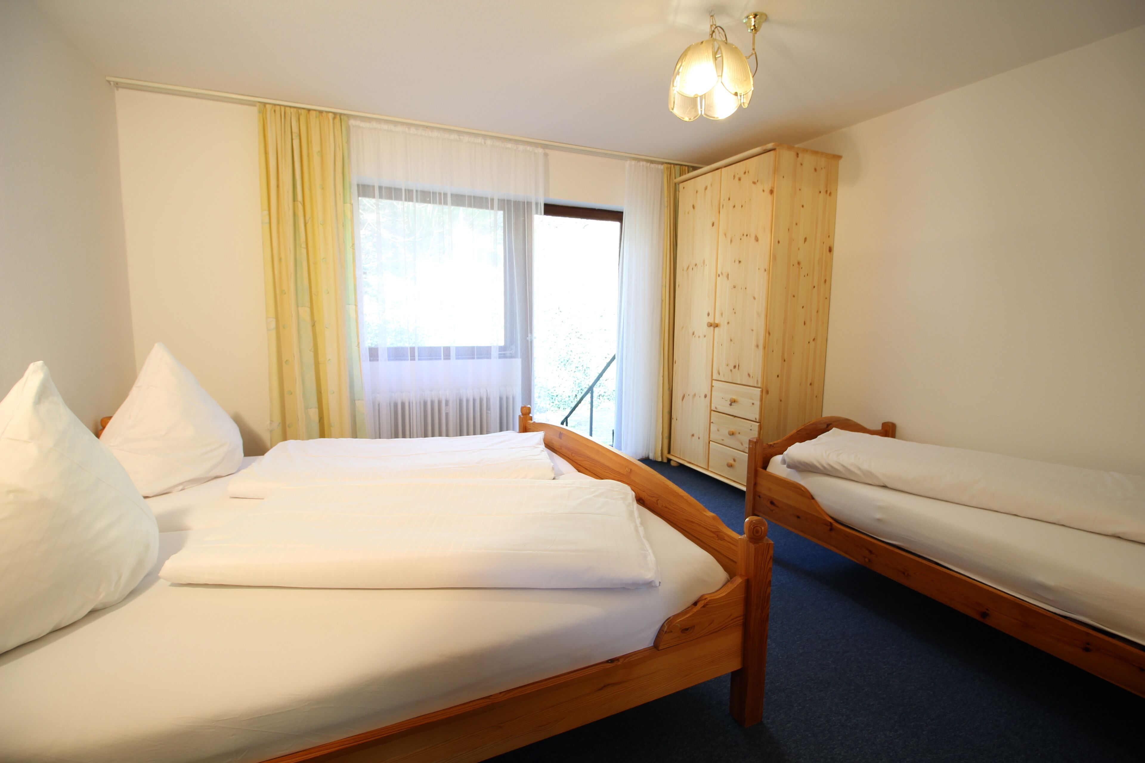 A room with two wooden beds, a wooden wardrobe, and a window with curtains.