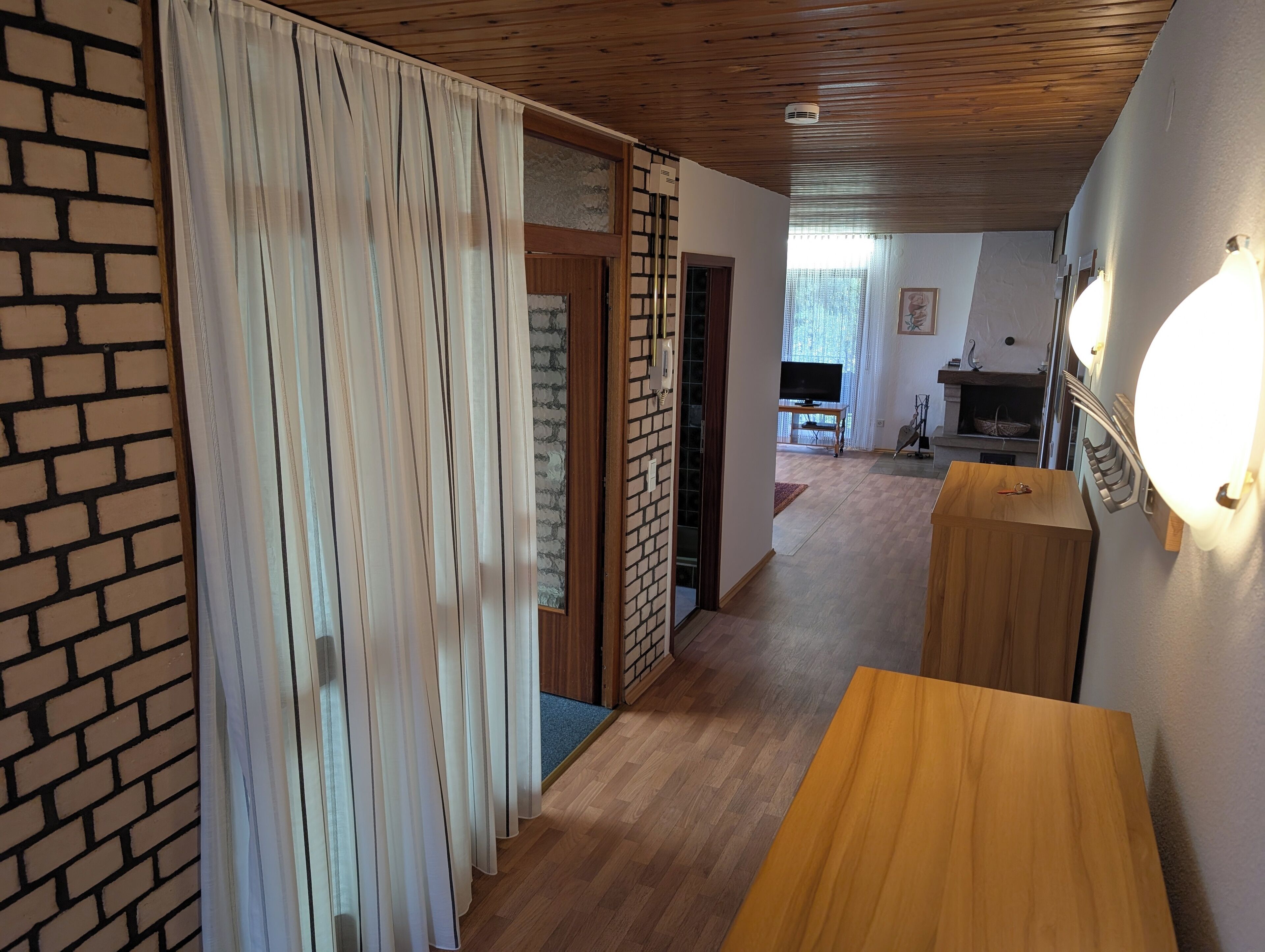 A hallway with wooden flooring, a brick wall, and a wooden door with curtains.