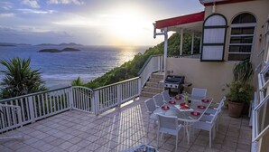 A terrace with a view of the sea, white outdoor furniture, and a barbecue area. - Casa de Suenos | St. John (Coral Bay)