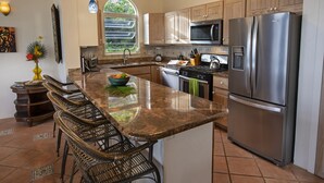 A kitchen with a central island, stainless steel appliances, and a view of greenery through a window. - Casa de Suenos | St. John (Coral Bay)