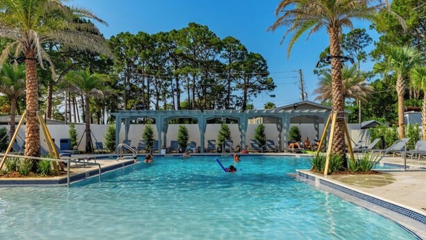 A swimming pool with clear blue water, surrounded by palm trees and a covered seating area.