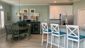 A kitchen with a dining table, chairs, a refrigerator, and artwork on the walls.