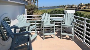 A balcony with Adirondack chairs and a table, overlooking a golf course and ocean.