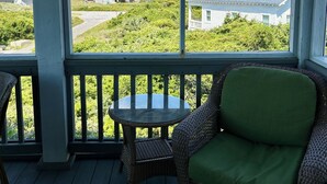 A covered porch with wicker furniture, a small table, and a view of houses and greenery. - NOW AVAILABLE LABOR DAY, OCEAN views, 2 KING masters. 2 clubs- separate purchase (Bald Head Island)