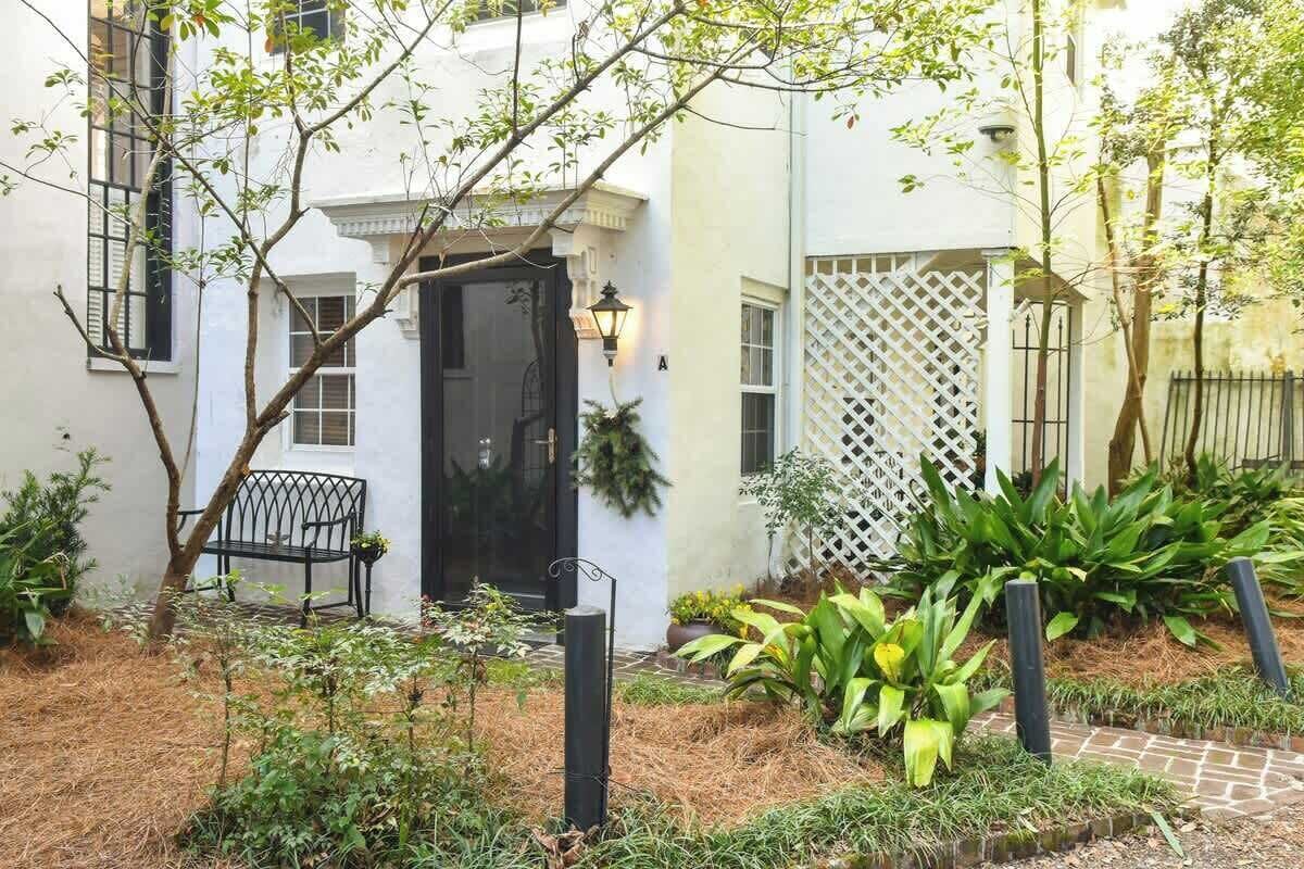 A white building with a black door, a bench, and a garden with plants and a pathway.