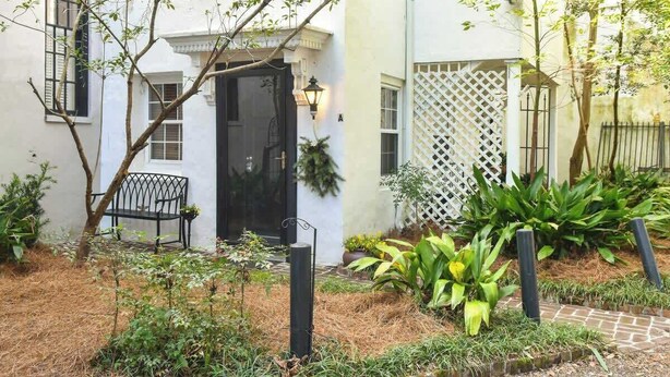 A white building with a black door, a bench, and a garden with plants and a pathway.