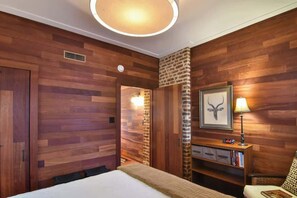 A hotel room with wooden panel walls, a bed, a nightstand with a lamp, and a framed picture on the wall.