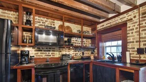 A kitchen with a brick wall, wooden cabinets, a microwave, a stove, and a sink. - The Coach House Circa 1755 (Charleston)
