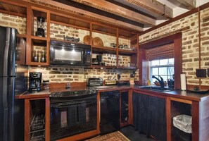 A kitchen with a brick wall, wooden cabinets, a microwave, a stove, and a sink.