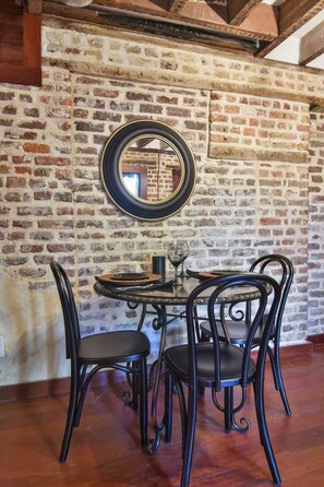 A rustic dining area with a brick wall, a round table, and black metal chairs. - The Coach House Circa 1755 (Charleston)
