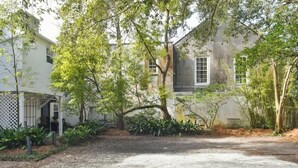 A residential property with a gravel driveway, mature trees, and a white building with a large window. - The Coach House Circa 1755 (Charleston)