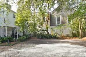 A residential property with a gravel driveway, mature trees, and a white building with a large window.