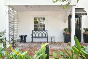 A covered patio with a bench, a small table, and potted plants.