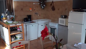 A compact kitchen with white appliances, a dining area with a table, and a chair. - Country cottage "Le Romarin" (Lagorce)