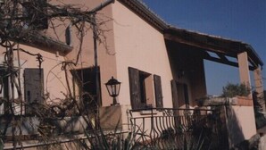 A building with a pink facade, wooden shutters, and a balcony with a metal railing. - Country cottage "Le Romarin" (Lagorce)