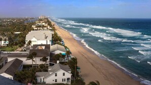 Un hotel frente al mar con edificios de varios pisos, una playa de arena y olas oceánicas.