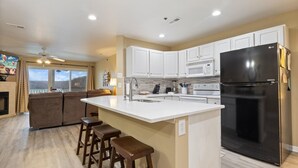 A modern kitchen with white cabinets, a black refrigerator, and a large island with stools. -  Parkview Bay 616, Book NOW for the SHOOTOUT RACE, VERY CLOSE TO RACE (Osage Beach)