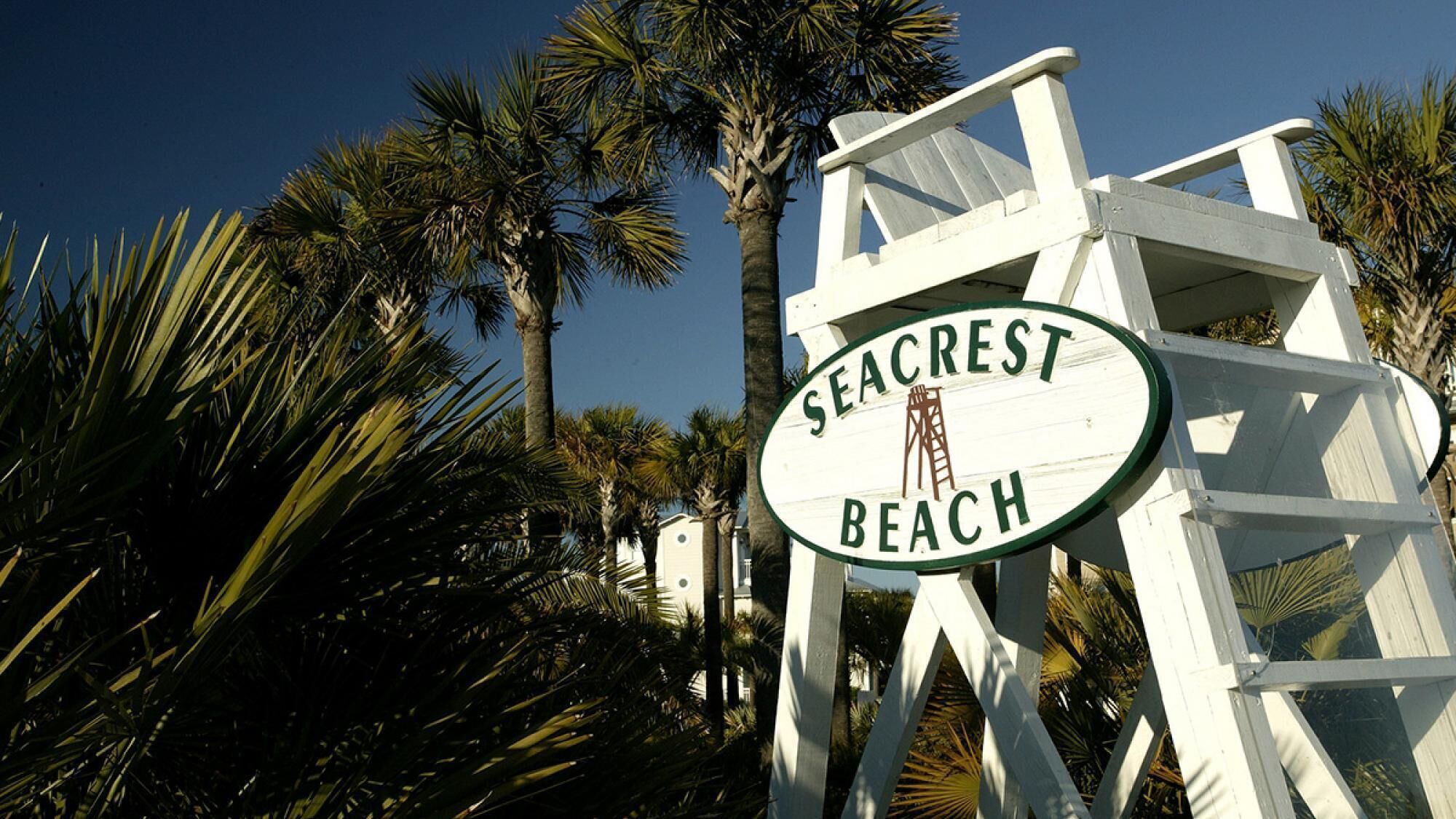 Schild für Seacrest Beach mit einer Palme und einer weißen Struktur im Hintergrund.