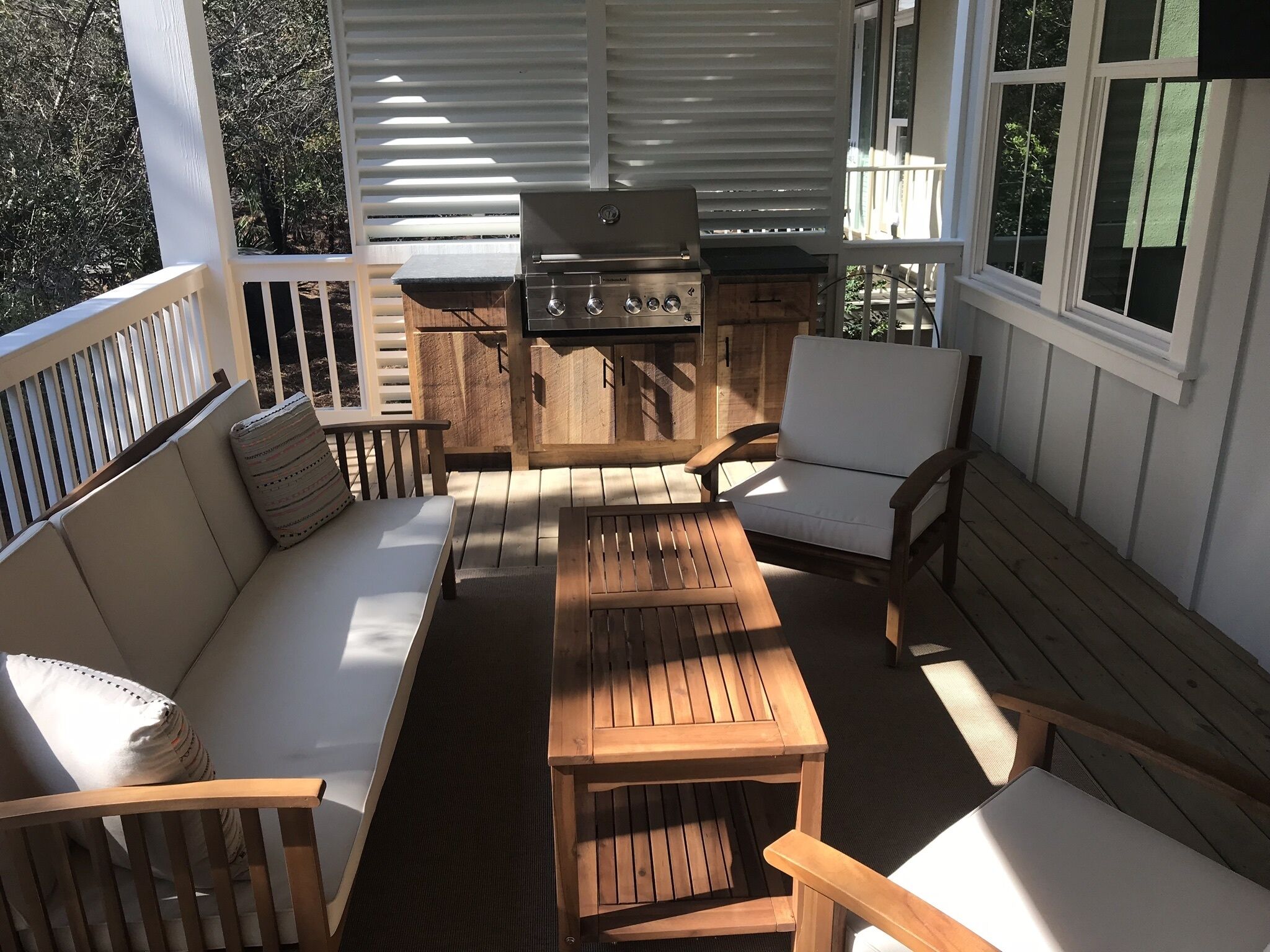 A covered outdoor patio with a wooden grill, seating area, and windows.