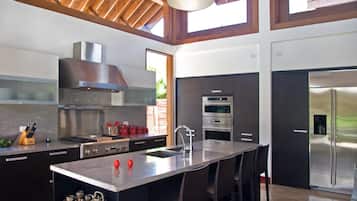 A modern kitchen with a central island, stainless steel appliances, and a high ceiling with wooden beams.
