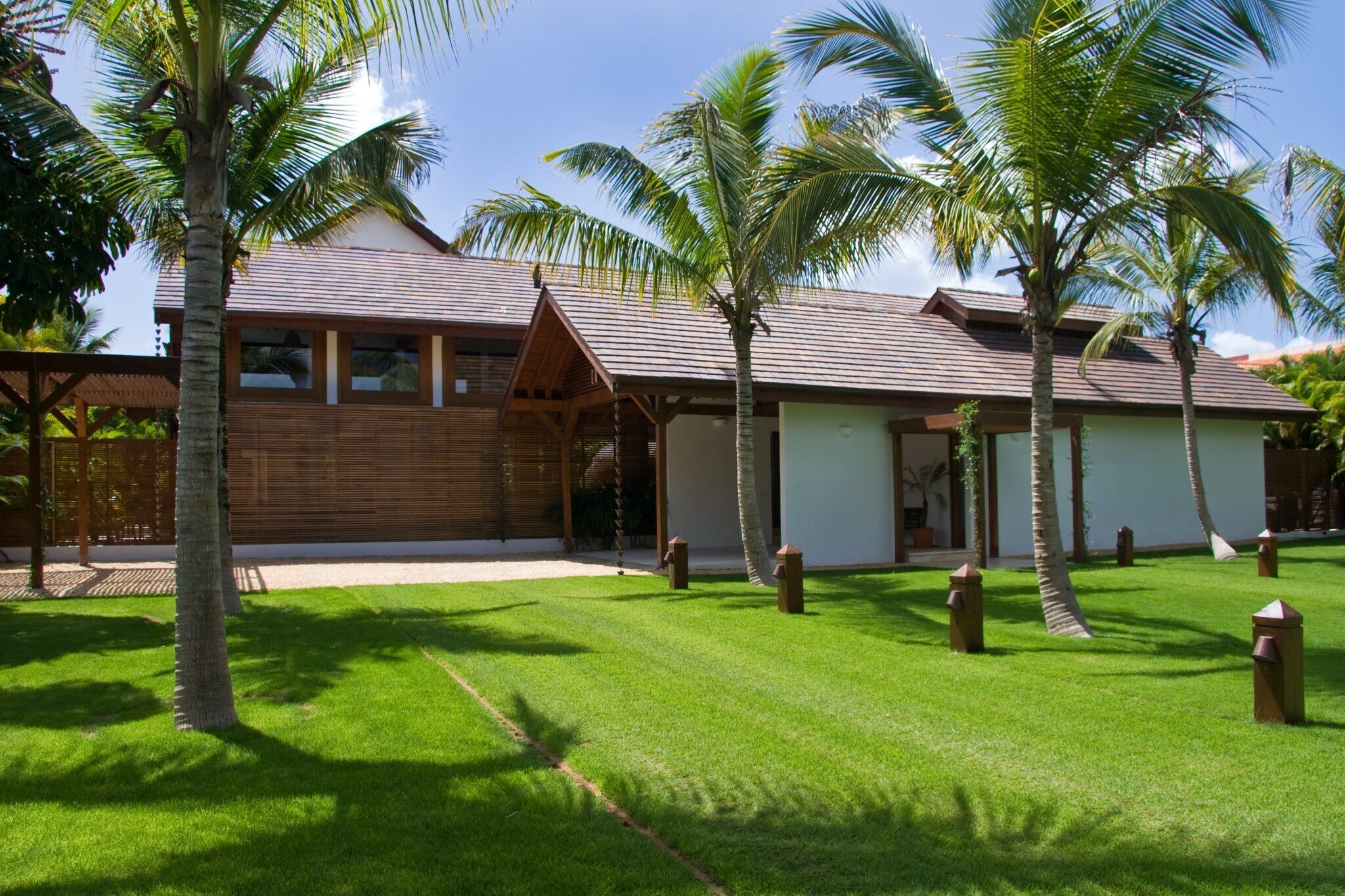 A resort with a wooden exterior, a covered outdoor area, and a well-maintained lawn with palm trees.
