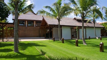 A resort with a wooden exterior, a covered outdoor area, and a well-maintained lawn with palm trees.