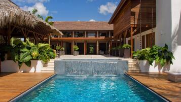 A swimming pool with a waterfall feature, surrounded by wooden deck and potted plants.