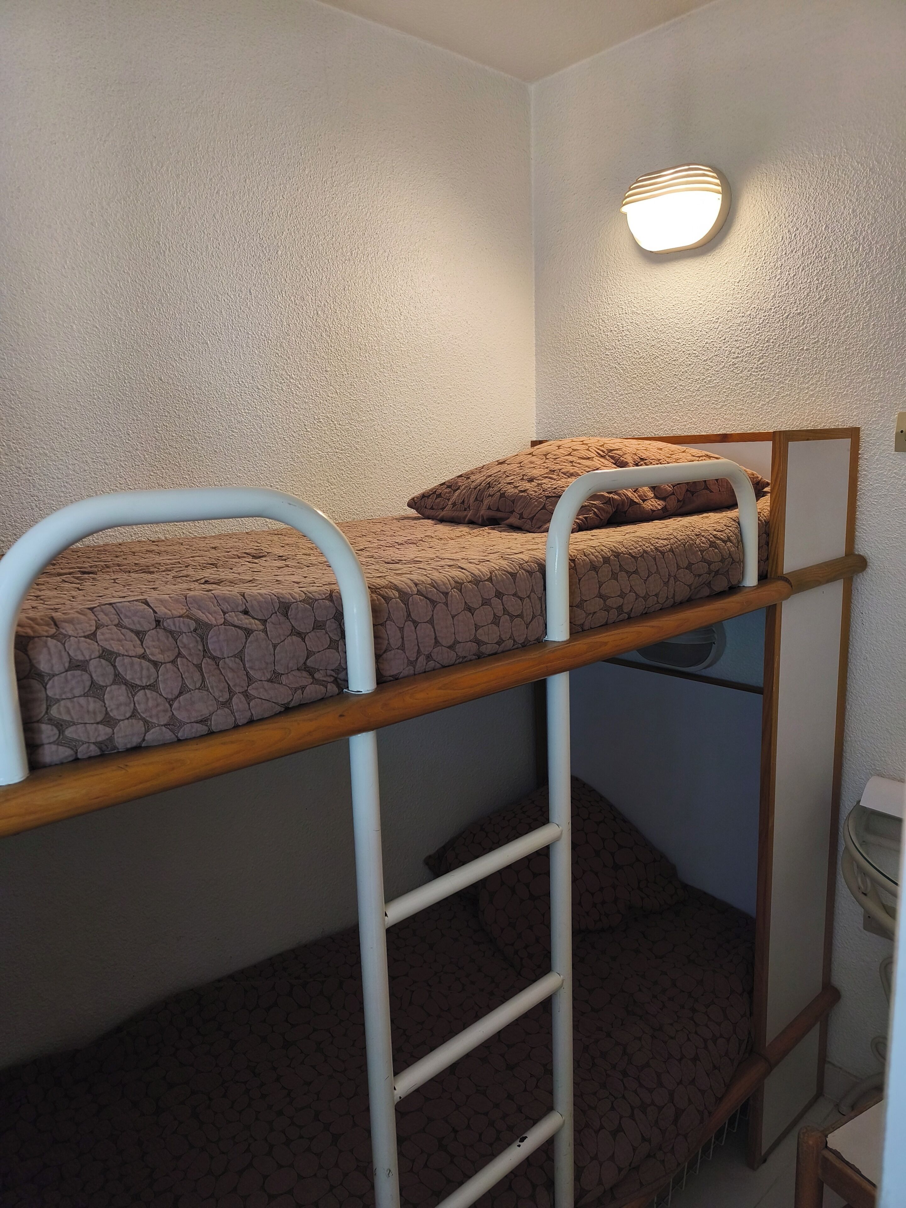 A bunk bed with a headboard, a ladder, and a wall-mounted light fixture.