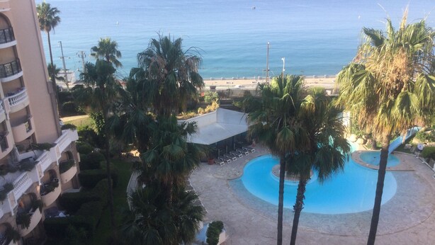 A resort with a pool, palm trees, and a view of the ocean.