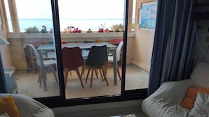 A modern living room with a glass coffee table, a sofa, and a view of the sea through large windows.