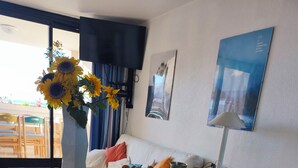 A modern living room with a glass dining table, white sofa, and a vase of sunflowers.