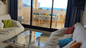 A living room with a sofa, a coffee table, and a view of the sea through large windows.