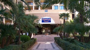 A hotel entrance with a sign for Maeva, surrounded by palm trees and a paved pathway.