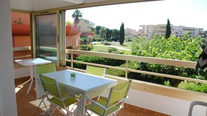 Ein Balkon mit Tisch und Stühlen, Blick auf einen Garten, und ein Gebäude im Hintergrund.