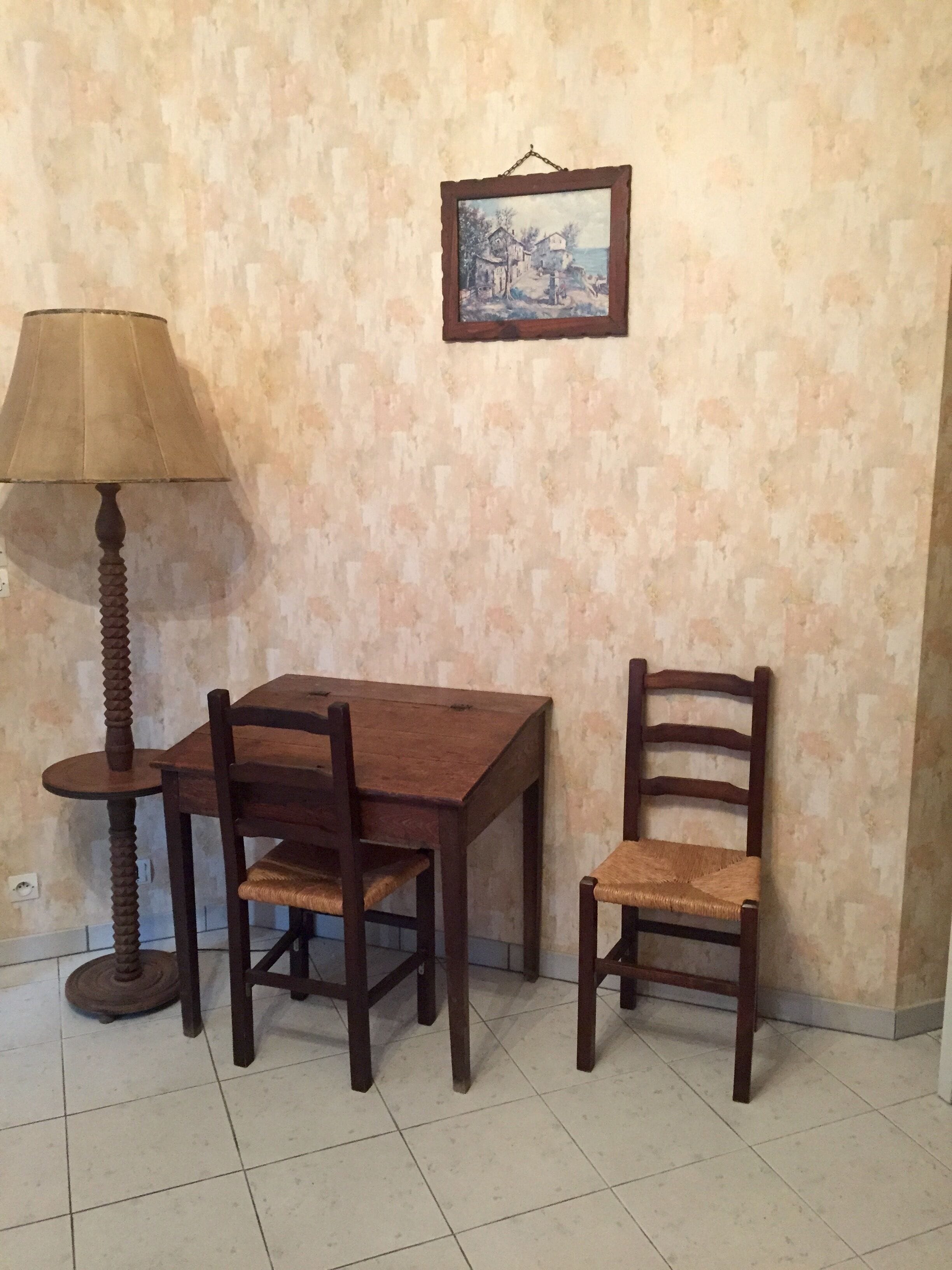 A dining area with a wooden table and chairs, a lamp, and a framed picture on the wall.